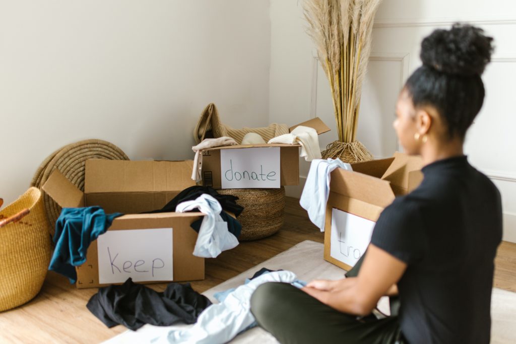 Woman sat on floor decluttering by organising things into a keep donate and throw boxes